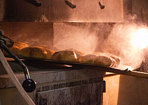 Die fertig gebackenen, noch heiß dampfenden Brötchen werden mit einem Schieber aus dem Ofen geholt.