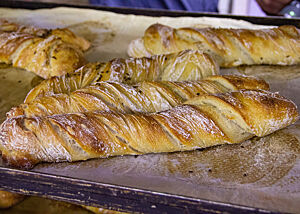 Goldbraun ausgebackene, gedrehte Brote mit leicht bemehlter Kruste liegen auf einem Backblech.