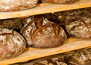 Kräftig ausgebackene Brote mit rustikal aufgerissener Kruste liegen in einem Holzregal.
