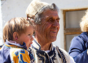 Anastas Karaj in seiner Tracht trägt ein Kind auf dem Arm.