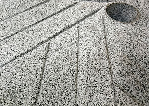 Ausschnitt von einem Mahlstein aus weiß-schwarz gesprenkeltem Granit mit Rillen in der Oberfläche.  