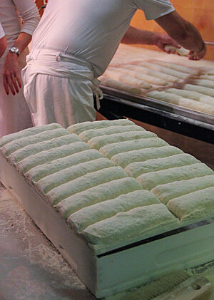 Ein Bäckermeister legt die fertig gereiften länglichen Teiglinge auf den Abziehapparat des Ofens.