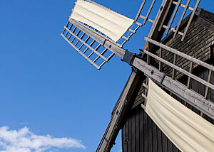 Die Flügel einer alten Mühle ragen in den blauen Himmel.