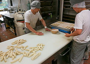 Zwei Bäcker schlingen die vorgeformten Teiglinge zu Brezeln.