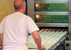 Die fertig gereiften und eingeschnittenen Baguetteteiglinge werden mit dem Abziehapparat in den Ofen geschoben. 