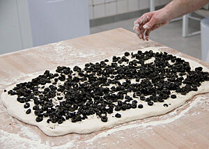 Der eckig ausgerollte Teig wird mit in Scheiben geschnittenen Oliven bestreut.