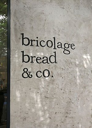Schwarze Schrift auf rauem Beton zeigt den Namen einer japanischen Bäckerei: „bricolage bread & co.“