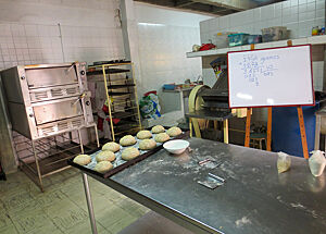 Im kolumbianischen Bäckereiklassenzimmer steht mitttig ein Tisch zum Herstellen und Bearbeiten des Teiges, im Hintergrund der Ofen zum Abbacken der Teiglinge.