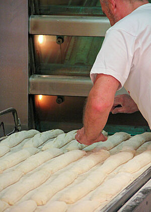 Ein Bäcker schneidet die fertig gereiften Baguetteteiglinge ein, bevor sie in den Ofen geschoben werden.