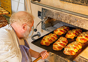 Der Bäckermeister Günther Weber holt ein Blech mit goldbraun gebackenen Hefezöpfen aus dem Ofen. 