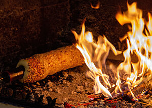 Ein um eine Holzstange gewickelter Skalický Trdelník wird nahe einer offenen Flamme gebacken.