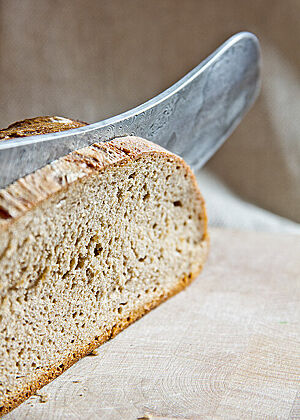 Das Damast-Brotmesser schneidet eine Scheibe Brot vom Laib ab.