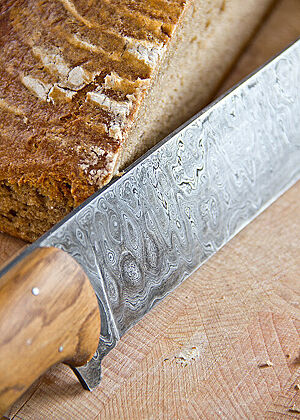 Die glänzende Klinge des Brotmessers liegt an einem angeschnittenen Brotlaib.
