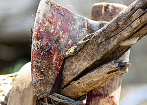 Eine blutverschmierte Axt hängt an einem Holzpfahl.