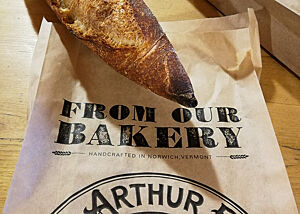 Ein rustikal ausgebackenes Baguette liegt auf einer Brottüte der King Arthur Bakery.