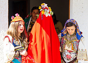 Bei der traditionellen Hochzeit steht die rot verschleierte Braut zwischen zwei Frauen in traditionellen albanischen Kleidern.