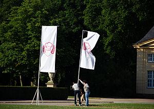 Weiße Fahnen mit dem rotem Emblem der Sendung „Deutschlands bester Bäcker“ werden aufgestellt.