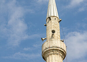 Der Turm einer Moschee in Tirana ragt in den blauen Himmel.