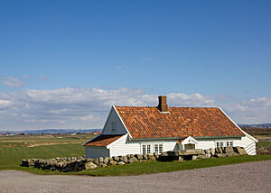 Typische norwegische Bauweise. Ein weißes holzverkleidetes Haus mit Sprossenfenstern, roten Dachpfannen und einem Steinwall ringsum.