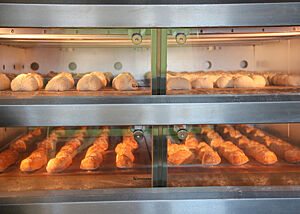 Der Blick durch die Glasscheibe zeigt den mit Baguettes und Weizenbrötchen beladenen Ofen.