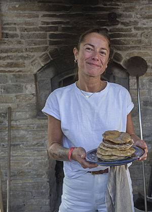 Eine Bäckerin hält lächelnd einen Teller mit gestapelten Fladenbroten in der Hand.