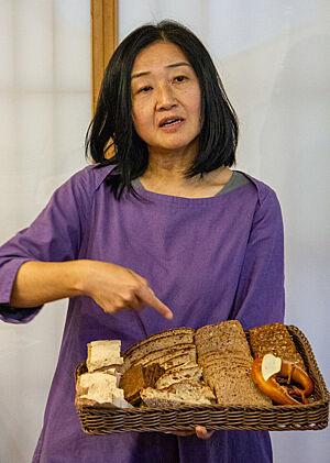 Tomoko Morimoto hält einen gut gefüllten Brotkorb in der Hand und zeigt auf ein Brot.