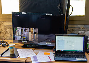 Auf einem Schreibtisch stehen Monitor, Laptop und einige Ausdrucke.