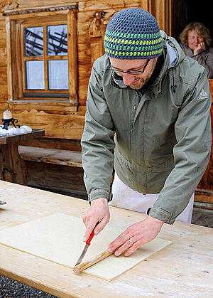 Mit Jacke und Mütze bekleidet schneidet Lutz Geißler vor der Almhütte auf einem Tisch Croissantteig.