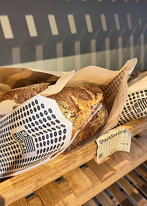Dieses Regal im Eingangsbereich von Bread 41 wird für Brote genutzt, die zur Abholung vorbestellt wurden. Ein Sauerteig-Saatenbrot liegt verpackt in einem Holzregal.