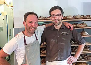 Pascal Rubertus und Lutz Geißler stehen vor einem Regal mit kräftig ausgebackenen Broten.