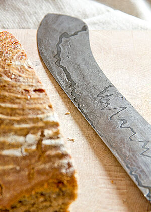Das Brotmesser mit sehr langer Klinge liegt neben einem angeschnittenen Brotlaib.