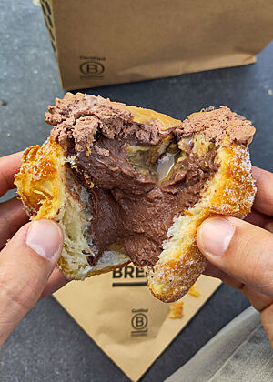 Innenansicht eines gefüllten Cruffins von Bread 41. Eigentlich schade um die Arbeit des Tourierens, denn angesichts der massiven Füllung fällt der Cruffin geschmacklich und haptisch gar nicht mehr ins Gewicht. Ein aufgerissener und mit Schokocreme gefüllter Cruffin.
