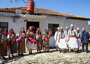 Traditionell gekleidete albanische Schäfer und ihre Frauen stehen vor einem Häuschen.