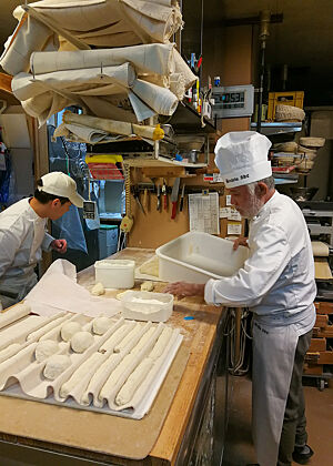 Herr Akashi beim Baguette-Formen. Bäcker Akashi formt auf der Arbeitsfläche Baguette-Teiglinge, die zur anschließenden Garei n Leinen gesetzt werden.