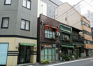 Altbestand in einer sehr schnell wachsenden und sich wandelnden Stadt. Zwischen und vor deutlich höheren Häusern steht ein nur zweigeschossiges altes Haus in Tokio.