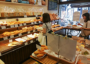 Zwei Kundinnen in einer Bäckerei in Tokio bedienen sich in der Auslage und bringen ihre Auswahl auf einem Tablett zur Kasse.