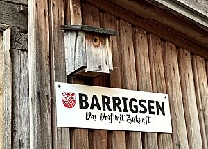 Unter einem an der Holzvertäfelung des Backhauses montierten Nistkasten hängt ein Schild mit der Aufschrift „Barrigsen Das Dorf mit Zukunft“.