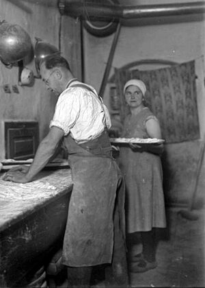 Auf dem Schwarzweißbild von ca. 1930 wirkt ein Bäcker einen Teigling; im Hintergrund eine Frau mit einem Tablett oder Ofenschieber, auf dem weitere Teiglinge liegen. (Bildnachweis: Deutsche Fotothek / Krauße, Hermann).
