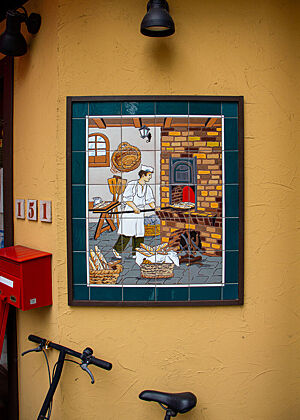 Wandbild aus Kacheln Das Bild zeigt einen Bäcker, der Teiglinge in den Holzofen schiebt.
