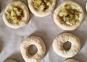 Bialys und Bagels während der Stückgare. Belegte Bialys (oben) und Bagels liegen auf Backpapier zur Gare.