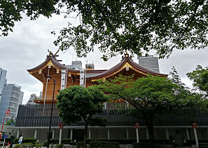 Ein kürzlich erdbebensicher sanierter buddhistischer Tempel in Tokio. Hinter kleineren Bäumen sind das Dach und Teile eines buddhistischen Tempels sichtbar.