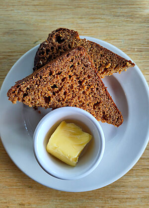 Das Treacle Bread im Restaurant The Woollen Mills in Dublin. Zu zwei Dreiecken halbierte Scheibe Rübensirup-Brot liegt mit etwas Butter auf einem Porzellanteller.