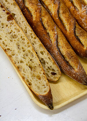 Mit Absicht flachgedrückt Baguettes, eines davon der Länge nach aufgeschnitten, auf einem Tablett.