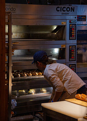 Eine Bäckerin schaut in den Etagenofen und prüft den Zustand der darin befindlichen Baguettes.