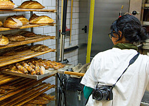 Zayaan holt die fertig gebacken Baguettes mit einem großen Schieber aus dem Ofen und legt sie zum Auskühlen in ein Ablageregal.