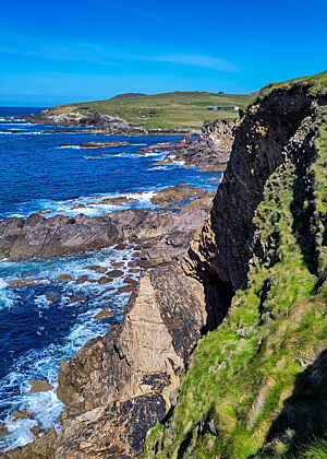 Blick auf den Atlantik in Dunquin auf der Dingle-Halbinsel. Azurblaues Meerwasser, aus dem Sandstein-Felsen ragen.