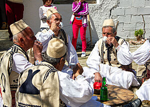 Die ihre traditionelle Tracht gekleidete Schäfer sitzen im Kreis auf dem Boden und trinken selbstgebrannten Schnaps aus kleinen Tassen.