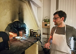 Ich beim Fladenbrotbacken im Holzofen. Lutz Geißler holt mit einem Holzschieber ein Fladenbrot aus dem Holzofen.