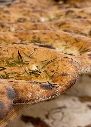 Eine Art Focaccia. Die Focaccia sind mit Rosmarinnadeln und Knoblauchzehen bestreut und glänzen von Olivenöl.