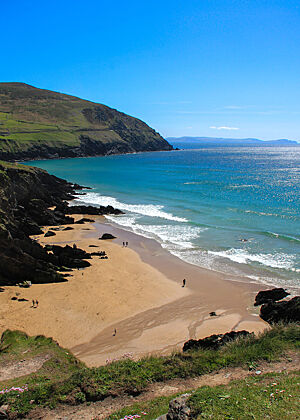 Kleiner Sandstrand an der Steilküste von Dunquin, Dingle-Halbinsel. Azurblaues Wasser am Sandstrand vor steil aufragenden Sandsteinen.